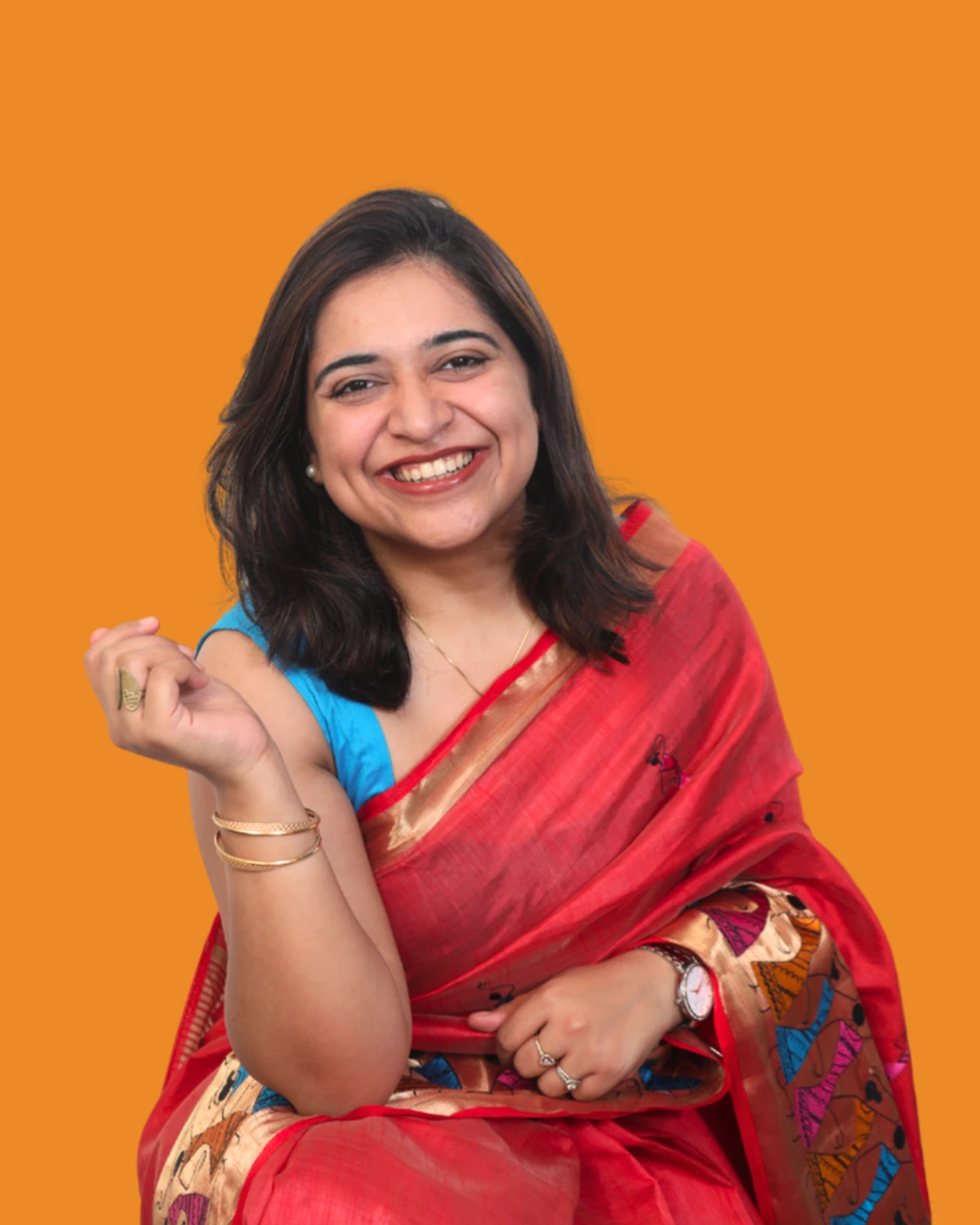 Shaurya Munjal smiling in a red saree against a bright orange background.